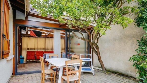 Een terras buiten met een tafel en stoelen, een overdekte zithoek en een boom.