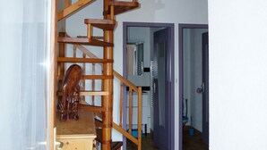 Een houten spiraaltrap in een kamer met betegelde vloeren en een houten kast.