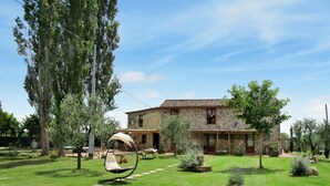 A stone house with a tiled roof, surrounded by a well-maintained lawn and trees.