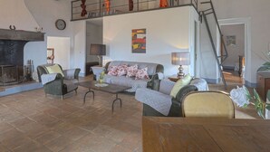 Un salón amplio con chimenea, un conjunto de sofás, una mesa de comedor y una escalera que lleva a un nivel superior.