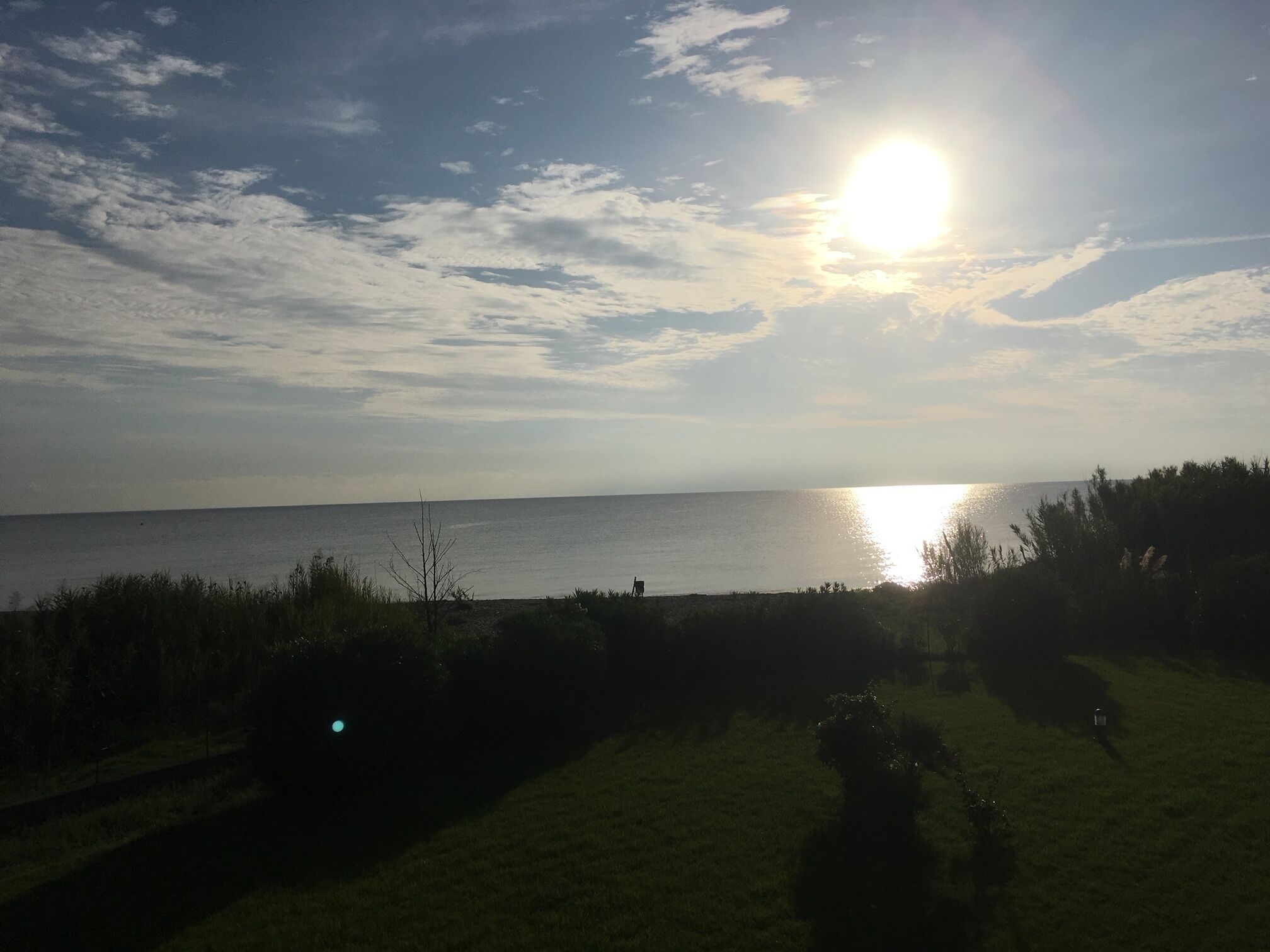A coastal landscape with a clear sky and the sun low on the horizon, reflecting on the water.