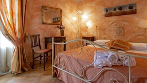 Un dormitorio con estructura de cama de metal, una silla de madera, una mesita de noche, un espejo y un cuadro en la pared.