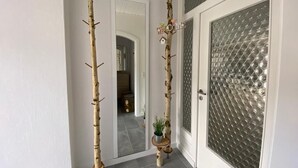 Een gang met een deur met een geëtste glazen ruit, een spiegel en een decoratieve boom met een 'WELCOME' bordje.