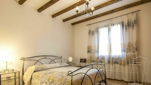 A bedroom with a bed, a nightstand, a chair, a hanging light fixture, and a window with curtains. - Nice apartment in villa for 7 people with WIFI, A/C, terrace and pets allowed (Pomarance)