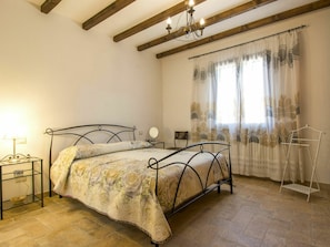 Een slaapkamer met een bed, nachtkastje, stoel, hanglamp en een raam met gordijnen.