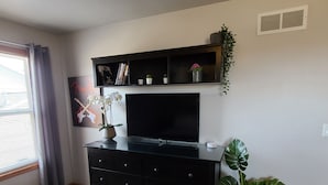 Una sala de estar con un mueble negro para el equipo de entretenimiento, un televisor de pantalla plana, una planta en maceta y una ventana con cortinas.