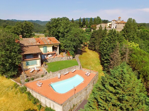 Eine Villa mit Schwimmbad, umgeben von üppiger Vegetation und einer Steinmauer.