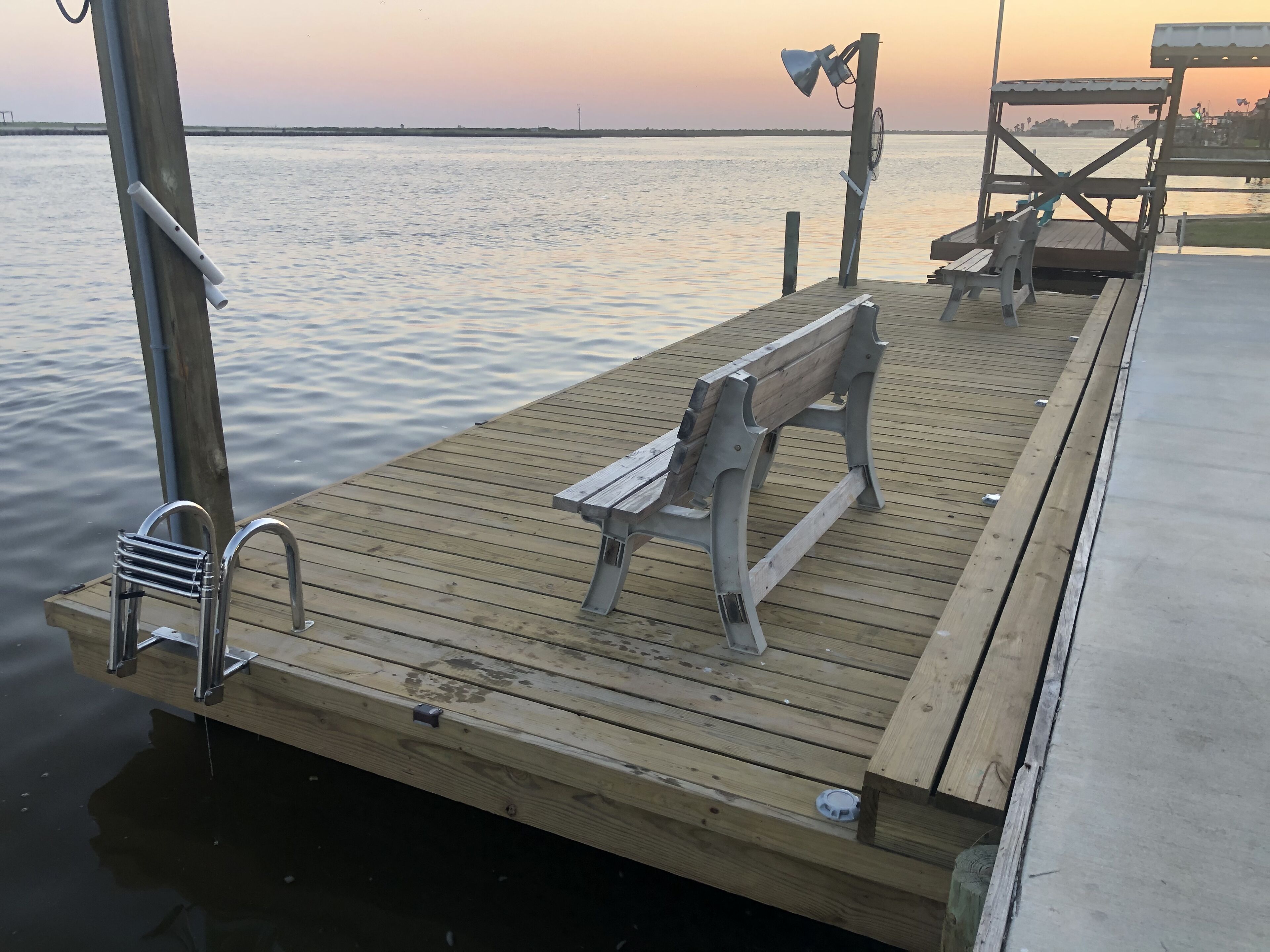 A wooden dock with a bench, a metal chair, and a bicycle rack.