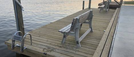 A wooden dock with a bench, a metal chair, and a bicycle rack.