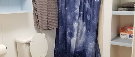 A bathroom with a toilet, a shower curtain with a galaxy pattern, a towel, and shelves with toiletries.