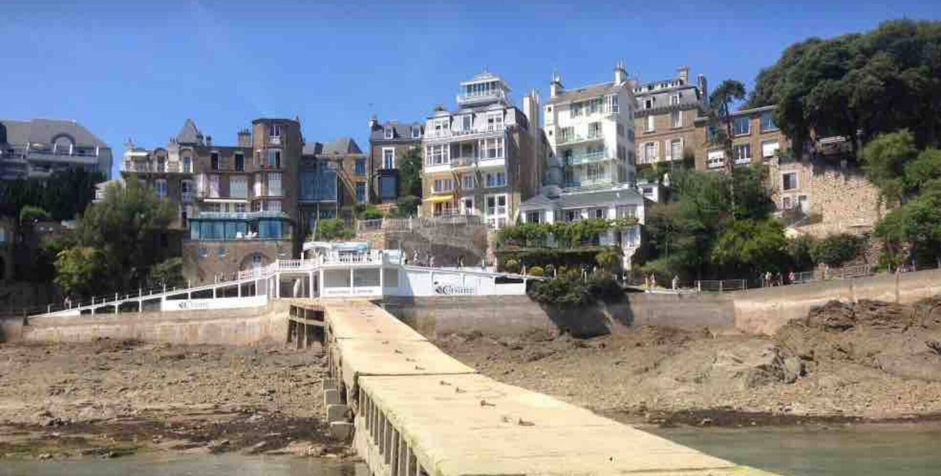 Une propriété située au bord de l’eau, dotée d’une longue jetée en bois qui s’avance dans une rivière, et entourée d’immeubles à plusieurs étages avec des balcons.