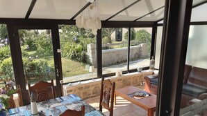 Eine sonnendurchflutete Terrasse mit einem Holztisch und Stühlen, einer Steinsitzbank und Blick auf einen Garten.