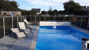 Ein Schwimmbecken mit Sicherheitszaun, Liegestühlen und blauem Himmel.