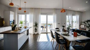 Een moderne keuken met een centraal eiland, een eethoek met een tafel en stoelen, en uitzicht op het omliggende landschap door grote ramen.