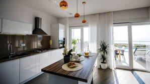 Een moderne keuken met een centraal eiland, hangende lampen en uitzicht op een balkon met zitplaatsen buiten.