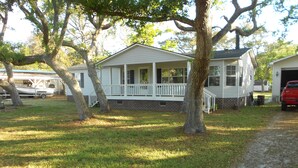 A single-story house with a porch, surrounded by trees and a gravel driveway. - Quiet 3 bedroom, 2 Bath Home located within 1/2 mile of ferry to Cape Lookout  (Harkers Island)