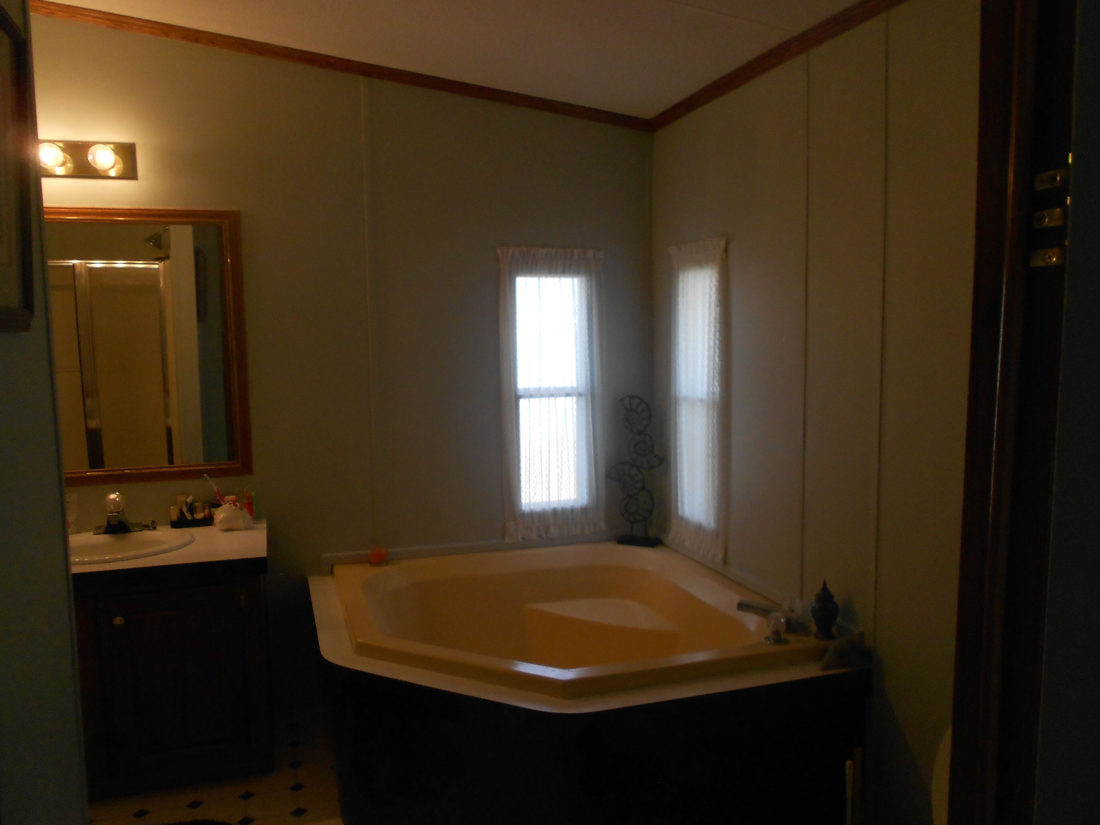 A bathroom with a large bathtub, a sink, a mirror, and a window with curtains.