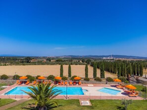 Un complexe hôtelier doté de deux piscines, de chaises longues et de parasols orange.
