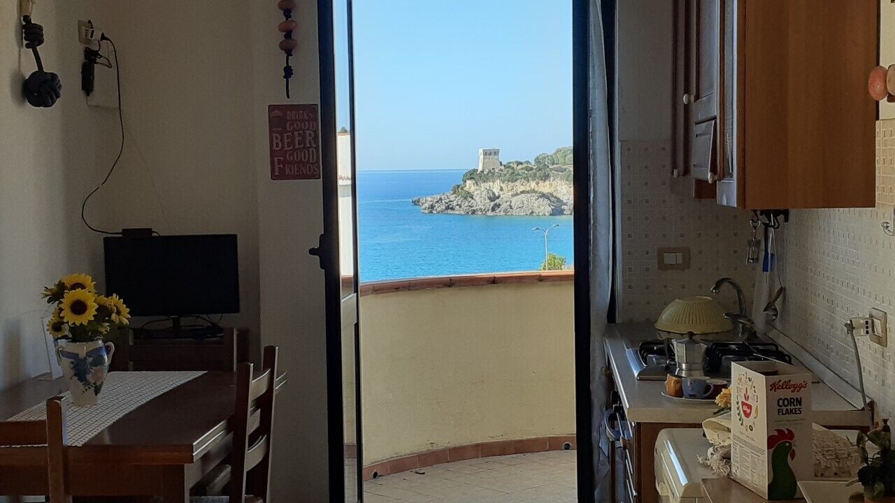 Une pièce avec vue sur la mer, un coin repas avec une table et des chaises, et une cuisine équipée d’un évier et d’une cuisinière.