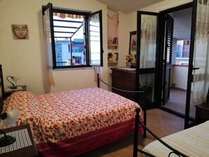 A bedroom with a bed, a desk, a chair, a window, and a door leading to a balcony. - Panoramic Apartment with two bedrooms  (Marina di Camerota SA)