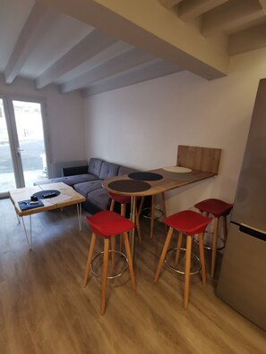 A modern living space with a sofa, a small table, red bar stools, and a refrigerator.