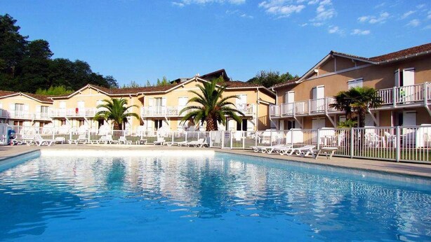 A swimming pool with lounge chairs and palm trees in front of a row of yellow buildings with balconies. - Duplex T3 Anglet - Parking / Terrace / Pool - (Anglet)