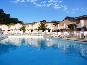A swimming pool with lounge chairs and palm trees in front of a row of yellow buildings with balconies.
