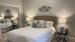 Un dormitorio con una cama grande, dos mesitas de noche con lámparas, un espejo y un adorno en la pared.