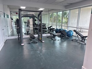 Ein Fitnessraum mit Trainingsgeräten, Bänken und großen Fenstern.