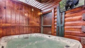 A wooden cabin interior with a hot tub, wooden walls, and a bear picture. - Day Dreamer by Beyond Expectations: Cozy Cabin w/ Views & Outdoor Fun (Gatlinburg)