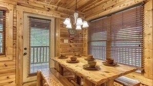 A wooden cabin with a large dining table, benches, and a chandelier. - Day Dreamer by Beyond Expectations: Cozy Cabin w/ Views & Outdoor Fun (Gatlinburg)