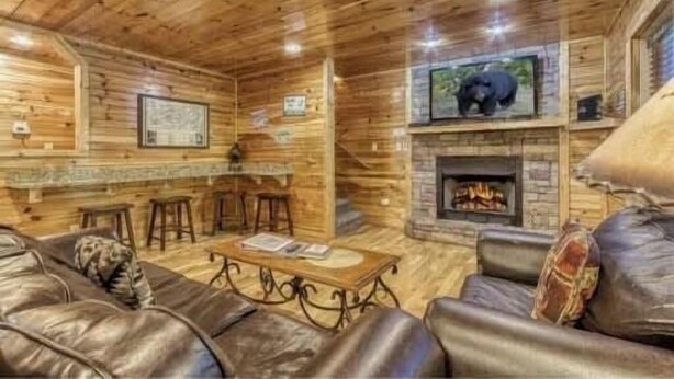 A cabin interior with a stone fireplace, leather sofa, and a bar area. - Day Dreamer by Beyond Expectations: Cozy Cabin w/ Views & Outdoor Fun (Gatlinburg)
