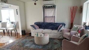 A living room with a white sofa, a blue sofa, a round coffee table, and a pink armchair. There is a window with a curtain, a door, and a small table with a radio. - Quaint Abingdon Cottage Downtown 420 East Valley Street  (Abingdon)