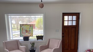 A room with two pink armchairs, a small table with a plant, a colorful artwork on the window, and a wooden door. - Quaint Abingdon Cottage Downtown 420 East Valley Street  (Abingdon)