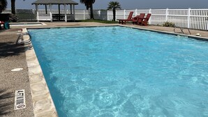 A clear blue swimming pool with a wooden deck, lounge chairs, and a gazebo.