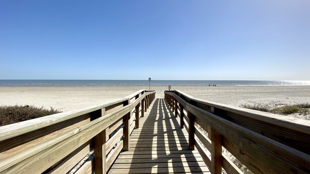 A wooden boardwalk leading to a beach with a clear sky.
