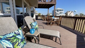 A covered outdoor deck with lounge chairs and a table, overlooking a residential area with houses and a water tower.