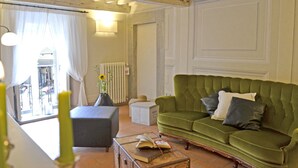 A cozy living room with a green sofa, a small table with a book, and a vase with a sunflower.