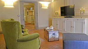 A living room with a green armchair, a blue ottoman, a television, and a cabinet with a candelabra.