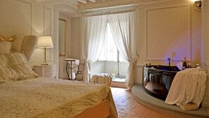 A bedroom with a bed, a vanity with a mirror, a bathtub, and a window with curtains.