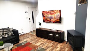 A living room with a black sofa, a TV mounted on the wall, a wooden floor, and a black cabinet. - Private Canoes & Charming Lake House  (Long Pond)