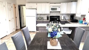 A dining table with chairs, a vase with flowers, and a kitchen in the background. - Private Canoes & Charming Lake House  (Long Pond)