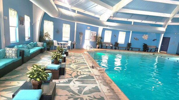 An indoor swimming pool with a blue wall, a seating area with cushions, and potted plants. - Private Canoes & Charming Lake House  (Long Pond)