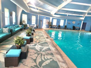 An indoor swimming pool with a blue wall, a seating area with cushions, and potted plants. - Private Canoes & Charming Lake House (Long Pond)