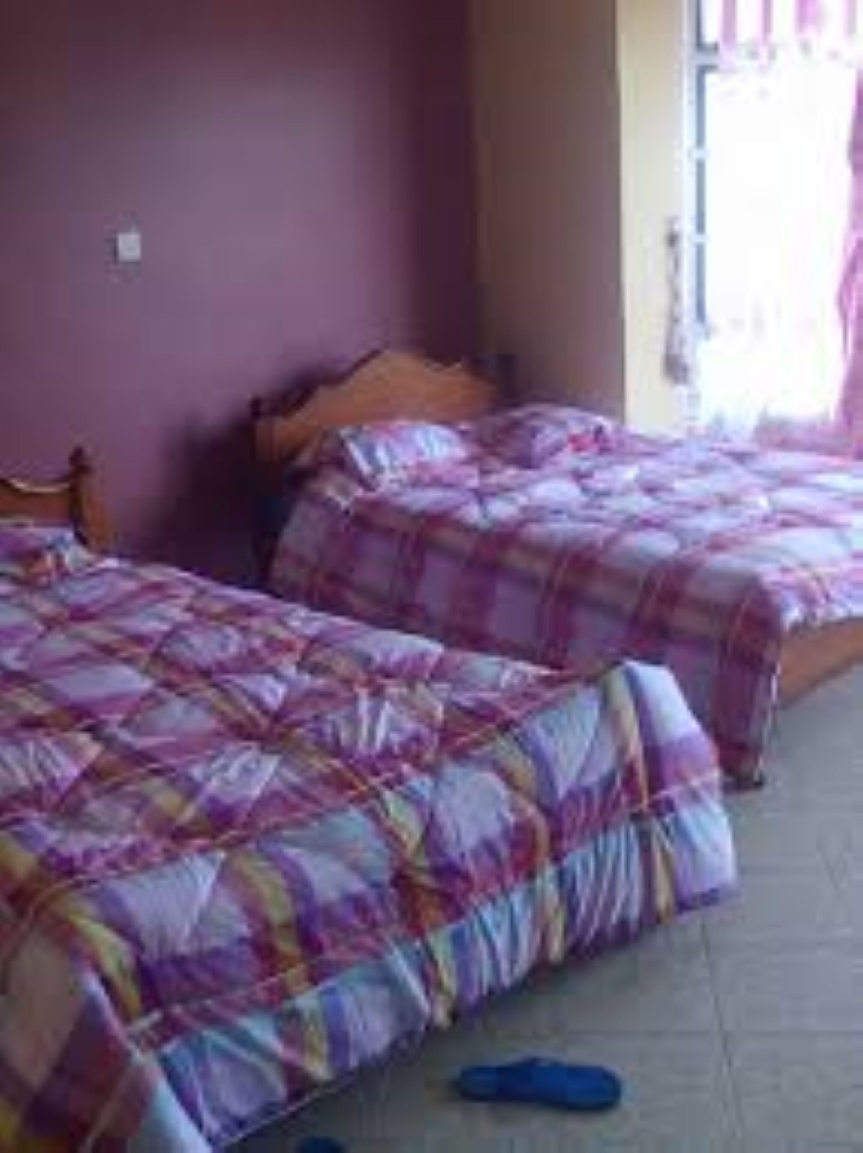 Una habitación con dos camas, cada una con una colcha de cuadros morados y rosados.