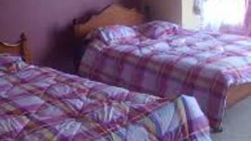 Una habitación con dos camas, cada una con una colcha de cuadros morados y rosados.