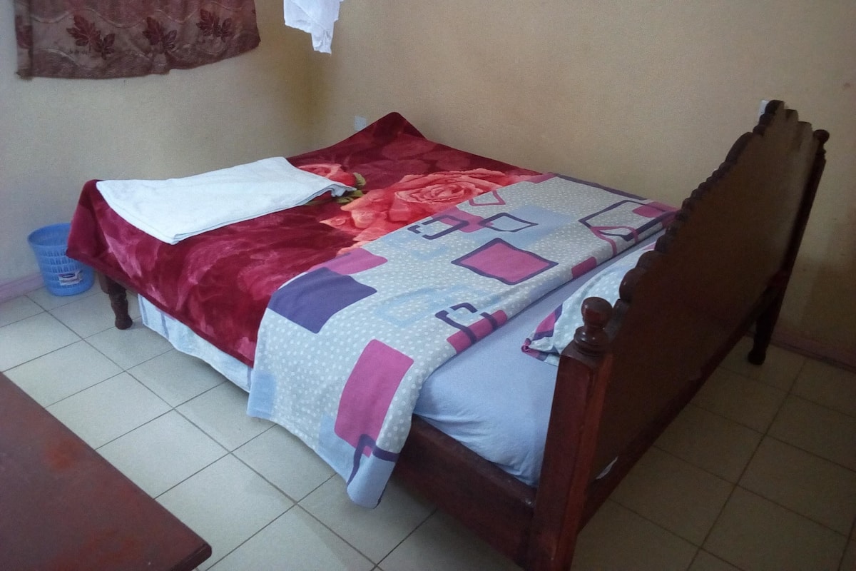 Una cama individual con edredón estampado con motivos florales, una colcha azul y rosa, y un cabecero de madera.