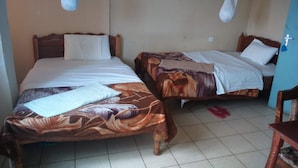 Two single beds with wooden frames and white bedding, a tiled floor, and a blue wall.