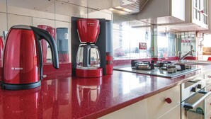 Una cucina con elettrodomestici rossi, tra cui una macchina per il caffè e un bollitore, e uno schienale in vetro.