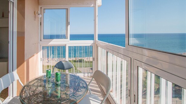 Un balcone con tavolo e sedie in vetro che si affaccia su una spiaggia e il mare.